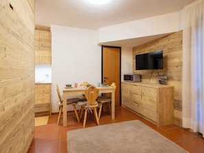Eine kleine Küche mit Holzausstattung, einem Esstisch mit Stühlen, einer Mikrowelle und einem an der Wand befestigten Fernseher.