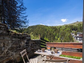 Eine Steinsäule, eine Holzbank, ein Tisch mit zwei Stühlen und eine herrliche Aussicht auf die Berge.