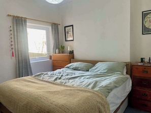 Ein Schlafzimmer mit Bett, Kommode, Lampe, einem Fenster mit Vorhängen und einer Karte an der Wand.