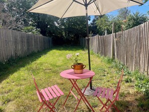 Ein Garten mit Holzlattenzaun, einem kleinen runden Tisch mit einem Blumentopf und zwei rosa Stühlen.