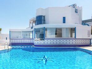Ein modernes Gebäude mit Schwimmbad, vor einem wolkenlosen, blauen Himmel, mit einem auf dem Wasserspiegel liegenden Sternfisch-Design.
