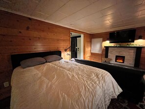 A room with wooden walls, a bed with white bedding, a fireplace, and a TV mounted above it. - Peaceful 1-bedroom cabin with cozy charm in Seattle, Full Kitchen, no clean fee! (Seattle)