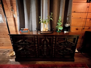 A wooden cabinet with decorative carvings, a vase with plants, a stack of books, and a small decorative tree.