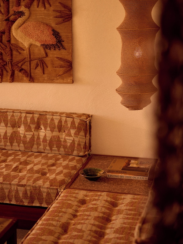 A room with a patterned sofa, a wall hanging, and a book titled 'Living by the Ocean' on a table. - The Whale (Narooma)