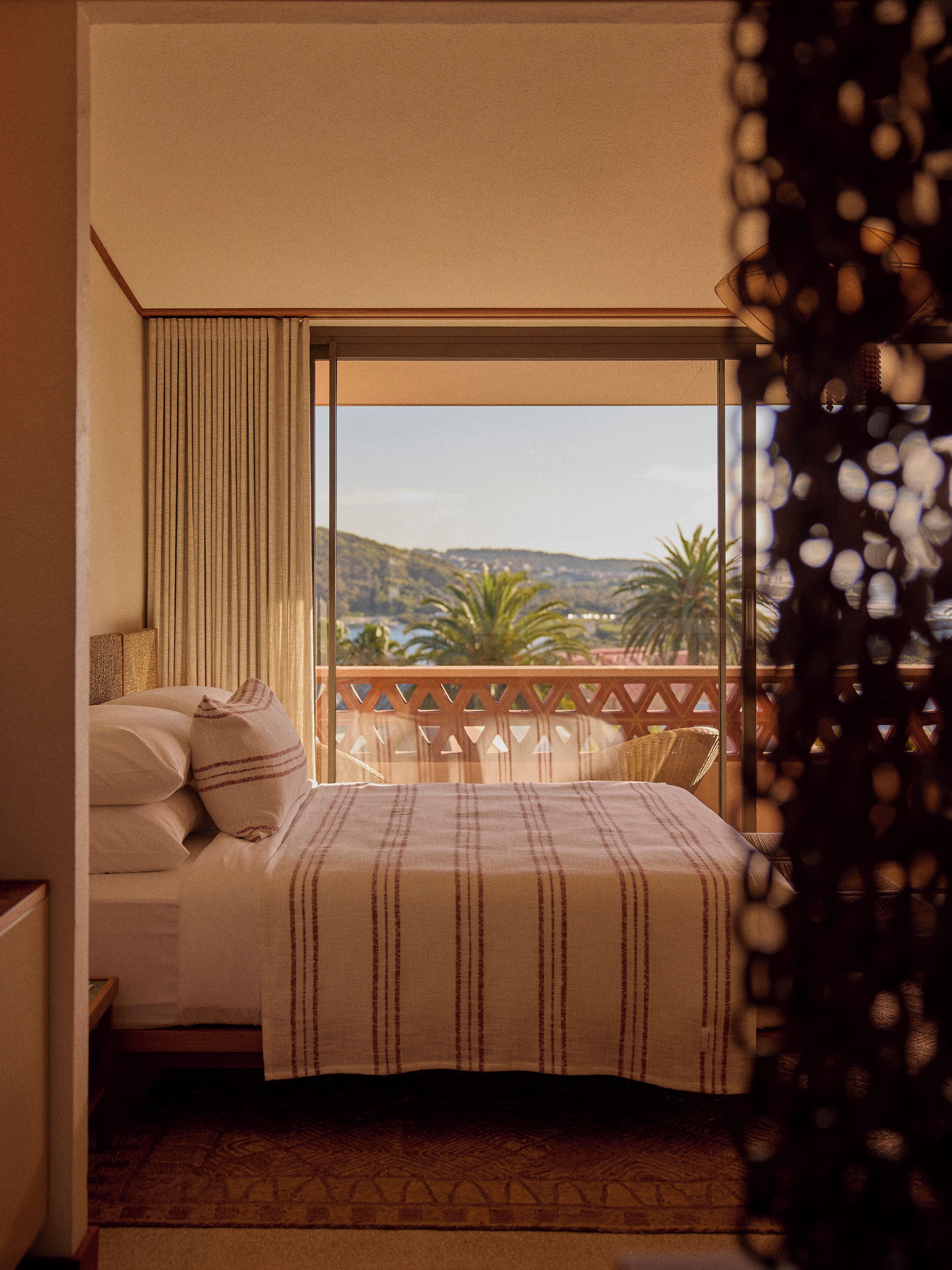 Quarto com cama, almofadas, vista para uma varanda e janela.