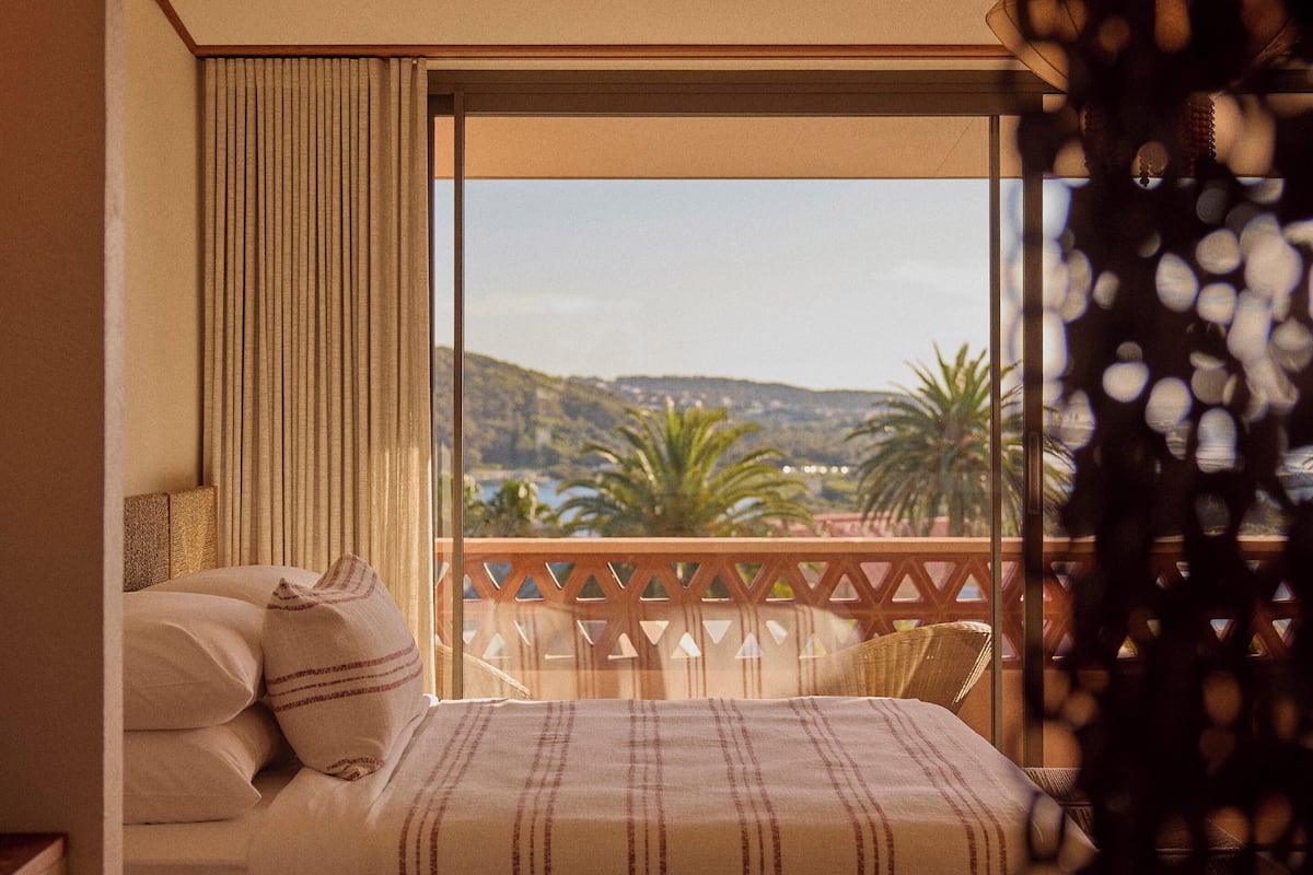 A bedroom with a bed, pillows, a view of a balcony, and a window.