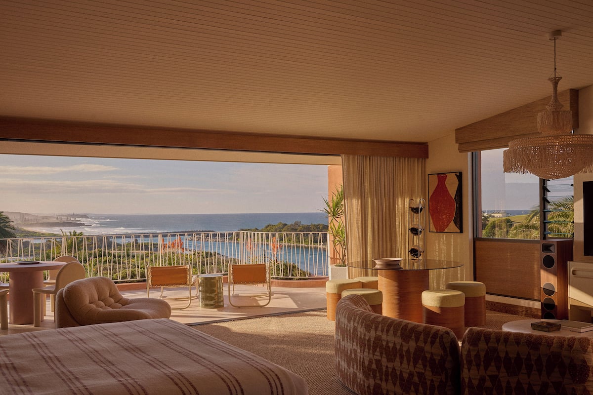A bedroom with a large window overlooking a scenic view, a bed, a seating area with chairs, and a small table.
