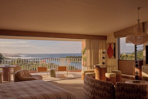 A bedroom with a large window overlooking a scenic view, a bed, a seating area with chairs, and a small table.