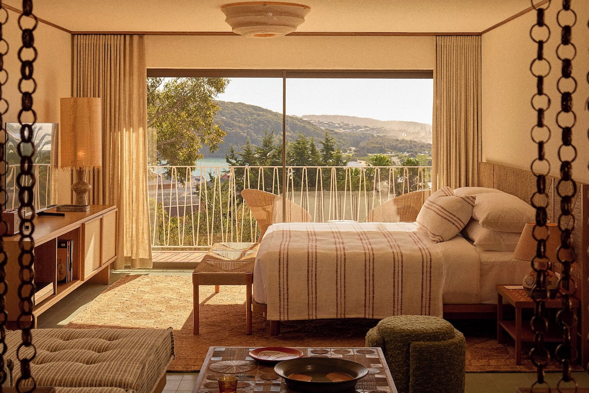A bedroom with a bed, bedside table, chair, and a view of the outdoors.