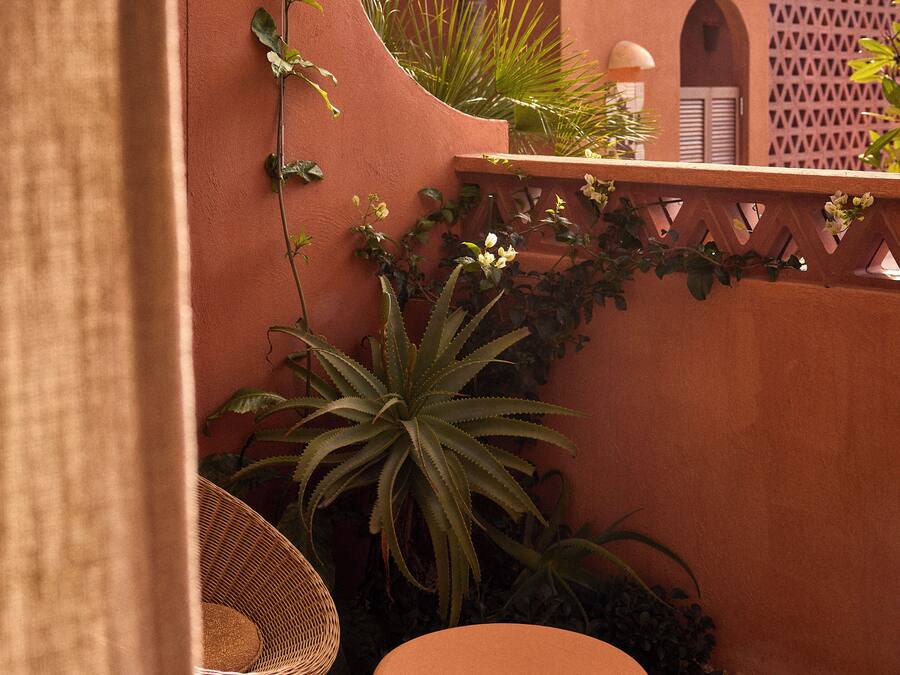 A cozy outdoor seating area with wicker furniture, a round table, and a variety of plants.