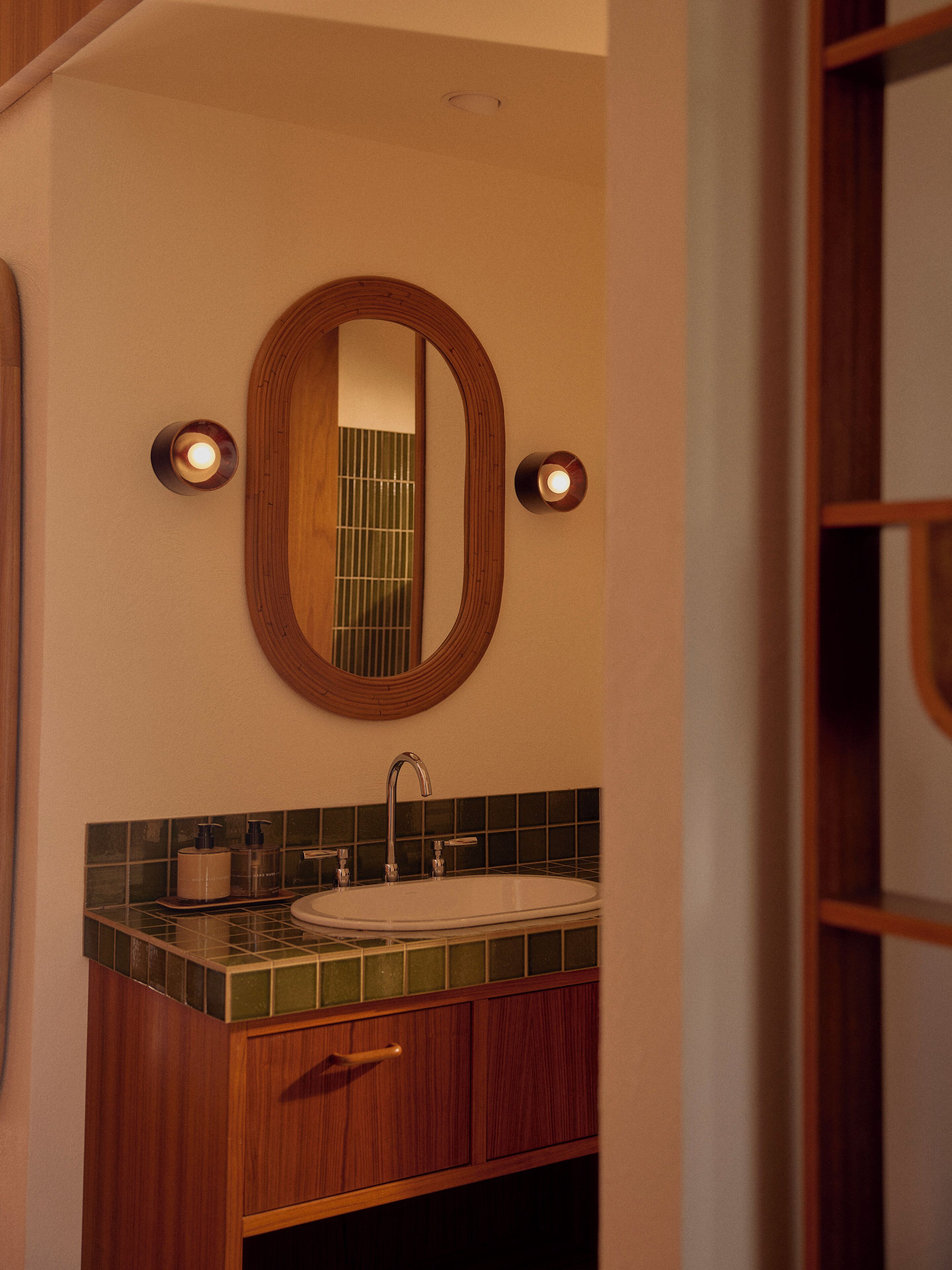 A bathroom with a wooden vanity, a white sink, and a mirror with two wall-mounted lights.