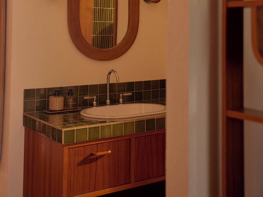 Un baño con tocador de madera, un lavabo blanco y un espejo con dos luces empotradas.