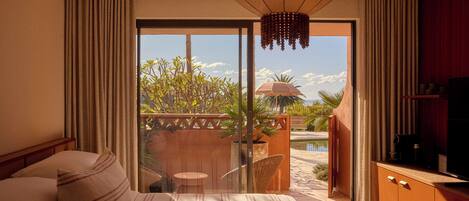 Une chambre d’hôtel avec un lit, une télévision et un balcon donnant sur la piscine et la verdure.