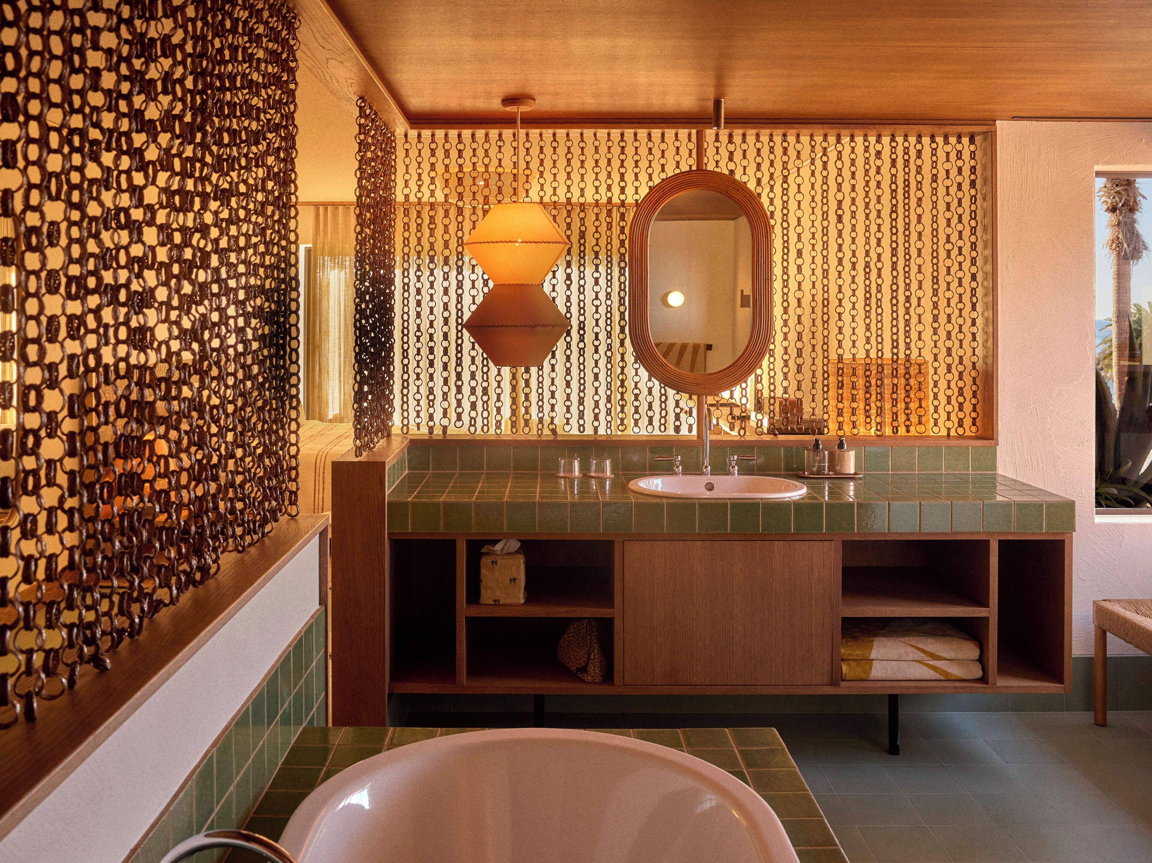 A bathroom with a green tiled sink, a wooden vanity, a large mirror, and a chain-link patterned wall.