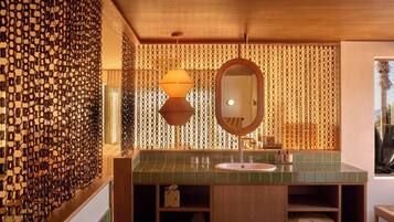A bathroom with a green tiled sink, a wooden vanity, a large mirror, and a chain-link patterned wall.
