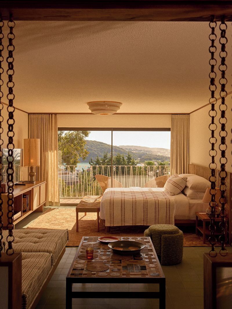 A bedroom with a bed, a table, a chair, a sofa, and a balcony with a view.