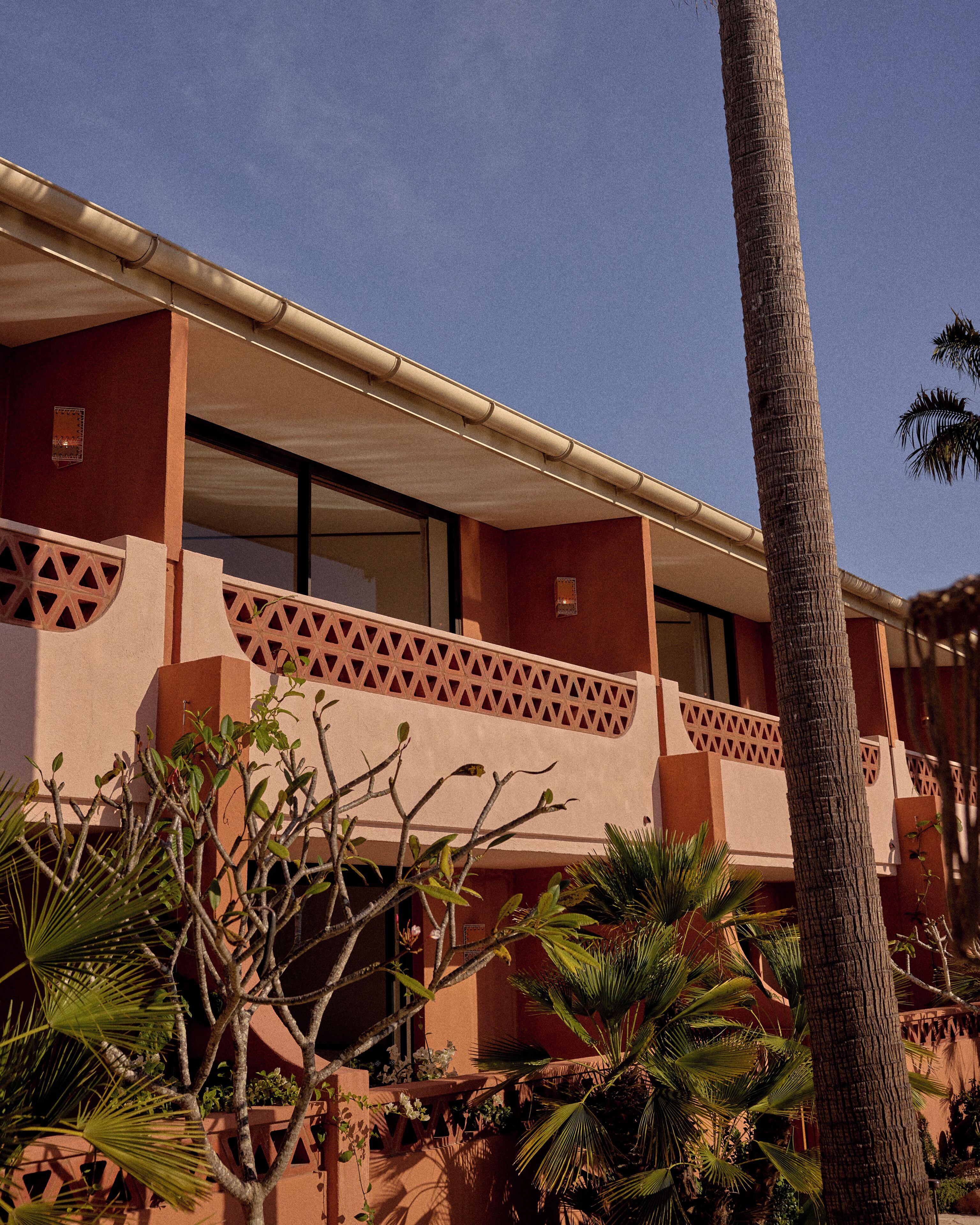 A building with a balcony, palm trees, and a clear sky.