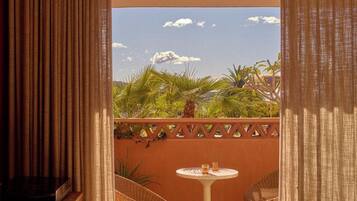 A room with a view of palm trees and a clear sky, a small round table, and two wicker chairs.