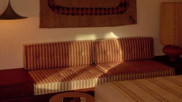 Una habitación con sofá, una mesa redonda, una lámpara colgante y un tapiz en la pared.