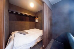 Ein Einzelbett mit Kissen, eine Pendelleuchte und ein Holzschrank in einem Zimmer mit dunkler Wand.
