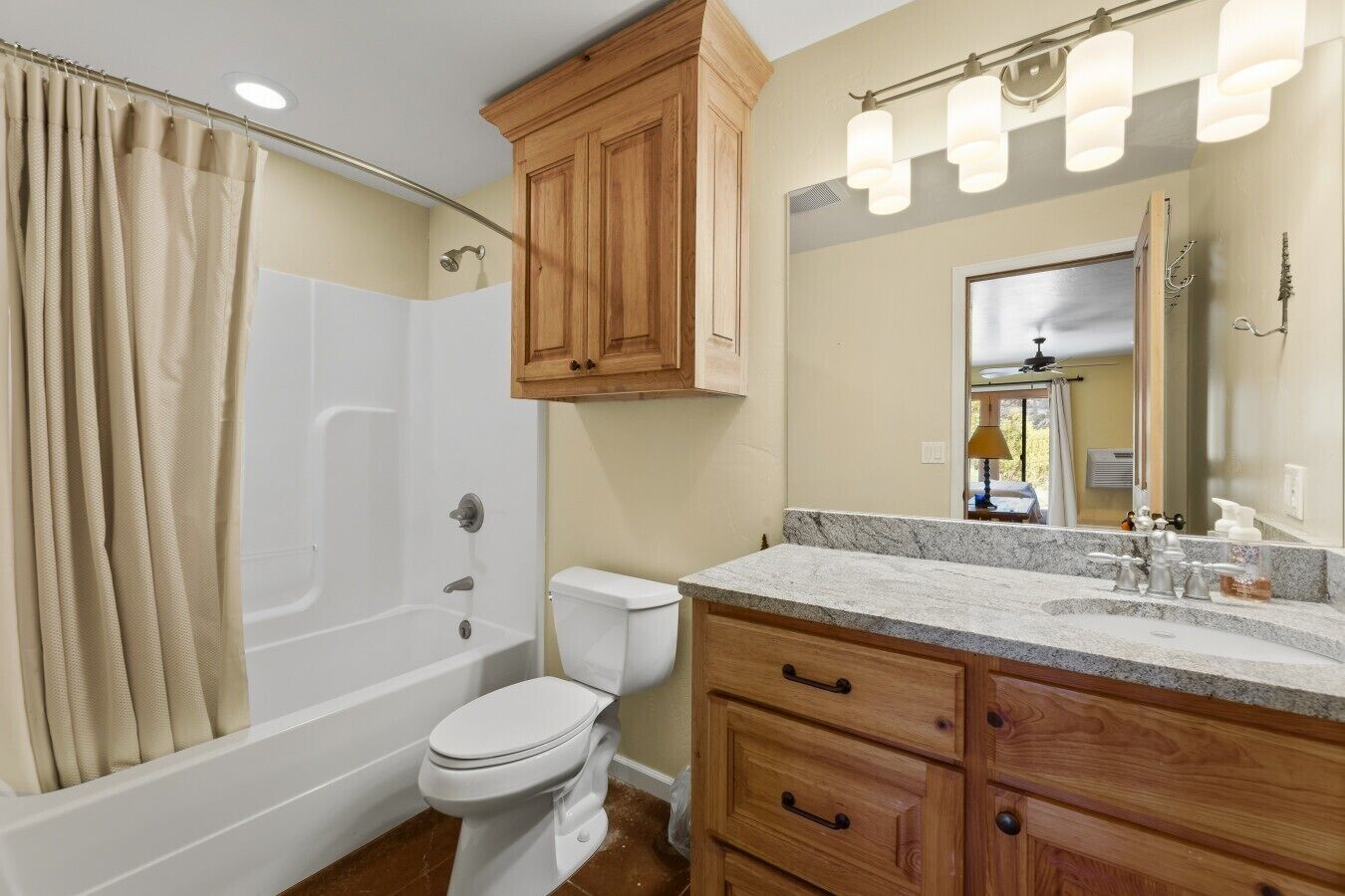 A bathroom with a bathtub, toilet, vanity with drawers, wooden cabinets, and a mirror.