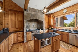 A kitchen with wooden cabinets, a stone fireplace, a stove, and a large window.