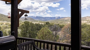 A wooden deck with a grill and chairs, overlooking a mountainous landscape with trees and a clear sky. - Secluded Mountain Ranch Home on 217 acres | Views | Fireplace | Hot Tub | Trout Pond (Silt)