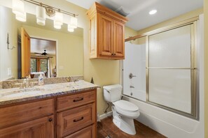 A bathroom with a wooden vanity, a toilet, a shower with a glass door, and a ceiling fan.