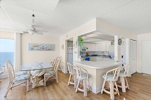 Une cuisine moderne avec des meubles blancs, un îlot central doté de tabourets de bar et un coin repas avec des chaises en osier.