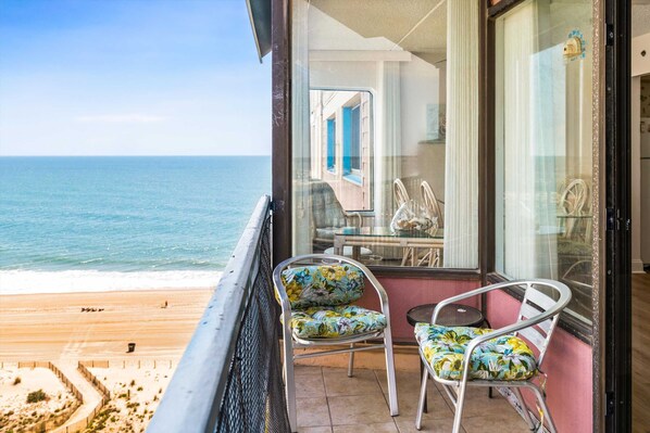 Un balcon avec deux chaises, une table et une vue sur la plage et l’océan.