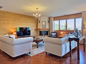 Ein Wohnzimmer mit zwei Sofas, einem Fernseher, einem Kamin, einem Couchtisch und einem großen Fenster mit Aussicht.