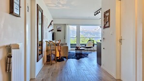 Une chambre d’hôtel moderne avec un plancher en bois, un coin repas comprenant des chaises et une table, un canapé et une grande fenêtre donnant sur la montagne.