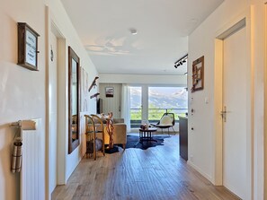 Ein modernes Hotelzimmer mit Holzboden, einer Essecke mit Stühlen und Tisch, einer Sitzecke und einem großen Fenster mit Blick auf die Berge.