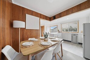 Een moderne keuken met houten lambrisering, een gedekte eettafel en een plant in pot, plus een koelkast.