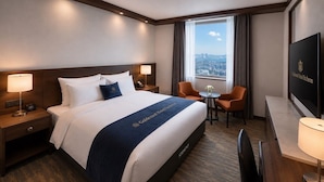 A hotel room with a large bed, two bedside tables with lamps, a desk with a chair, a television, and a window with a city view. - Goldcoast hotel Incheon (Incheon)