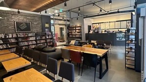 A modern cafe with wooden tables, black chairs, and bookshelves. - Goldcoast hotel Incheon (Incheon)
