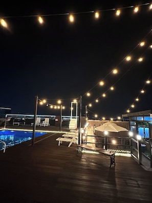 A poolside area with lounge chairs, a small table, and string lights.