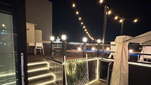A rooftop terrace with a white fence, string lights, and a covered area. - Goldcoast hotel Incheon (Incheon)