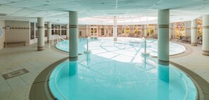 Ein großer, überdachter Schwimmbereich mit klarem Wasser, umgeben von Säulen, und eine Bank in der Nähe des Eingangs.