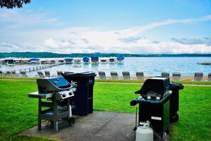 A lakeside view with a dock, lounge chairs, and barbecue grills.