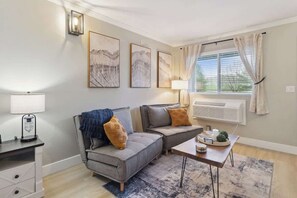 A living room with a grey sofa, a small table, a lamp, and a window with curtains.
