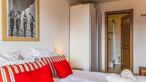 Een hotelkamer met een bed, kussens, een ingelijst kunstwerk, een kledingkast en een badkamers deur.