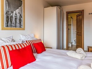 Ein Hotelzimmer mit Bett, Kissen, einem gerahmten Bild, einem Kleiderschrank und einer Badezimmertür.