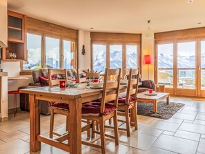 Ein Essbereich mit Holzmöbeln, einem Tisch für vier Personen und großen Fenstern mit Blick auf die Berge.