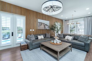 A modern living room with a sectional sofa, a wooden coffee table, and a large window with curtains. - Waverly Oasis at Destin Pointe | Private Pool, Resort Amenities & Beach Access (Destin)