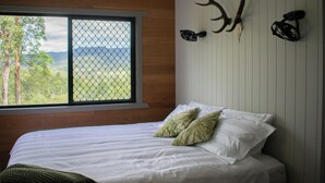 A bedroom with a bed, pillows, a window with a view, and wall-mounted antlers. - Tranquil secluded mountain chalet- perfect for relaxing! (Mount Byron)