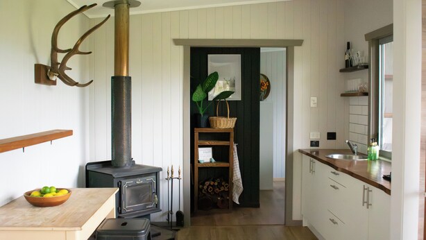A kitchen with a wood-burning stove, a bowl of fruit on the table, and a wooden bench. - Tranquil secluded mountain chalet- perfect for relaxing! (Mount Byron)