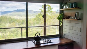 A kitchen with a large window, a kettle, and a plant on the counter. - Tranquil secluded mountain chalet- perfect for relaxing! (Mount Byron)