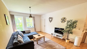 Ein modernes Wohnzimmer mit einer Couch, einem Couchtisch, einem Fernseher und einer Zimmerpflanze.