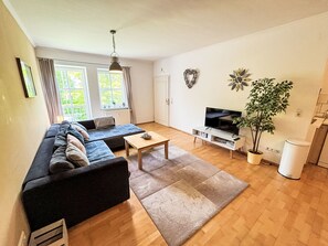 Ein modernes Wohnzimmer mit einer Couch, einem Couchtisch, einem Fernseher und einer Zimmerpflanze.